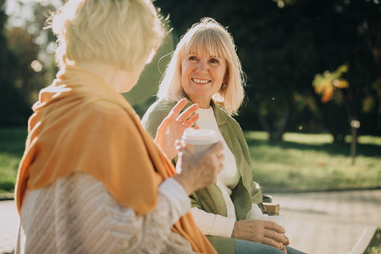 Elderly women talking and smiling in the park while drinking coffee